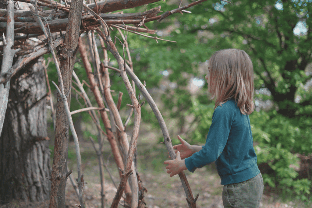 Kinder bauen eine Hütte im Wald aus Ästen und Laub.