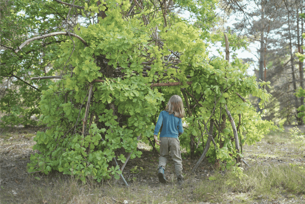 Kinder bauen eine Hütte im Wald aus Ästen und Laub.