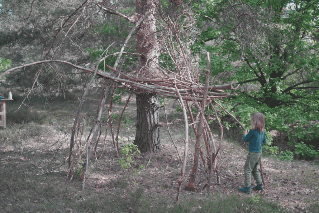 Kinder bauen eine Hütte im Wald aus Ästen und Laub.