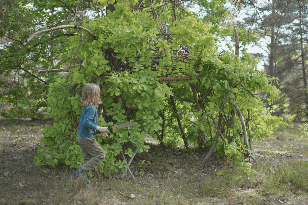 Kinder bauen eine Hütte im Wald aus Ästen und Laub.