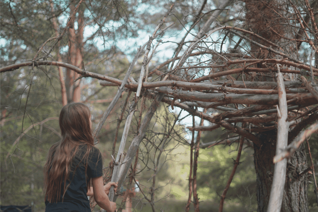 Kinder bauen eine Hütte im Wald aus Ästen und Laub.