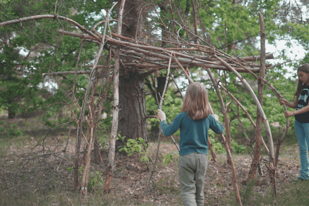 Kinder bauen eine Hütte im Wald aus Ästen und Laub.