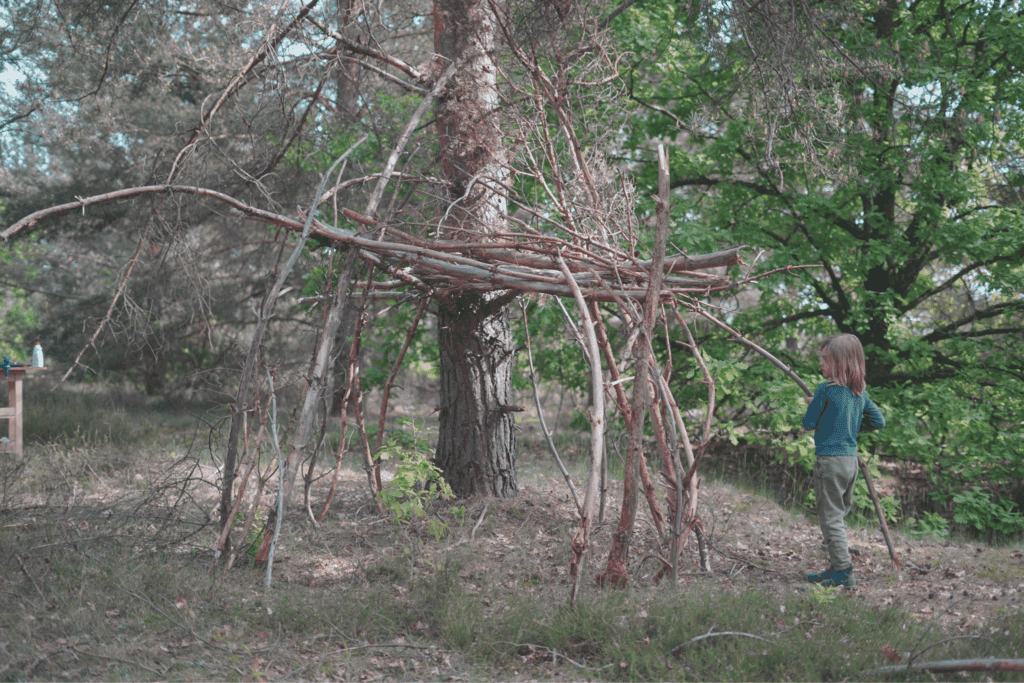 Kinder bauen eine Hütte im Wald aus Ästen und Laub.